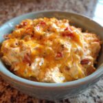 Close-up of creamy, cheesy rotel dip topped with melted cheddar and herbs in a light blue bowl.