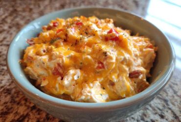 Close-up of creamy, cheesy rotel dip topped with melted cheddar and herbs in a light blue bowl.