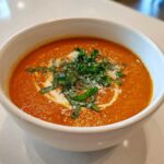 Close-up of a creamy bowl of tomato basil soup topped with fresh basil, Parmesan, and a swirl of cream.