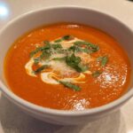 A close-up of a bowl of creamy tomato basil soup, garnished with basil and grated cheese.