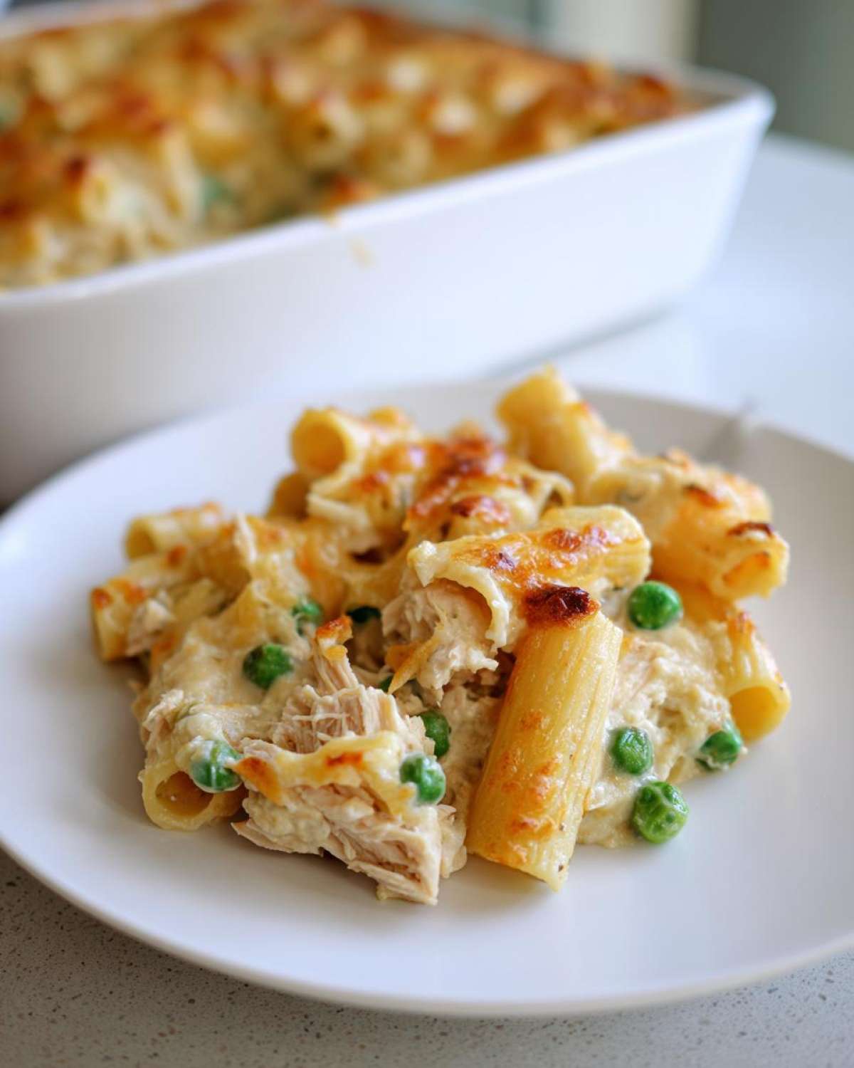 A serving of creamy tuna pasta with peas and a golden baked cheese topping on a white plate.