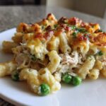 A close-up serving of creamy tuna pasta baked with a golden, bubbly cheese topping and green peas.