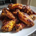 A close-up of a pile of golden brown, crispy baked chicken wings seasoned with spices.