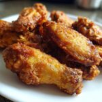 Close-up of several golden brown, crispy baked chicken wings piled on a white plate.