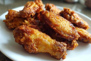 Close-up of several golden brown, crispy baked chicken wings piled on a white plate.