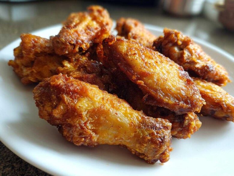 Close-up of several golden brown, crispy baked chicken wings piled on a white plate.