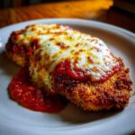 A close-up of a golden, breaded chicken parmesan recipe topped with melted, bubbly mozzarella cheese and marinara sauce.