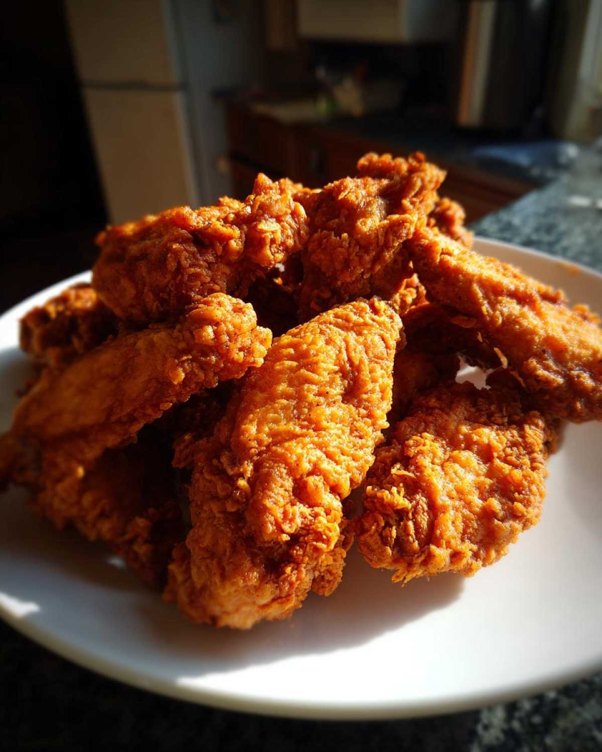 A pile of golden brown, crispy fried chicken wings resting on a white plate under dramatic lighting.