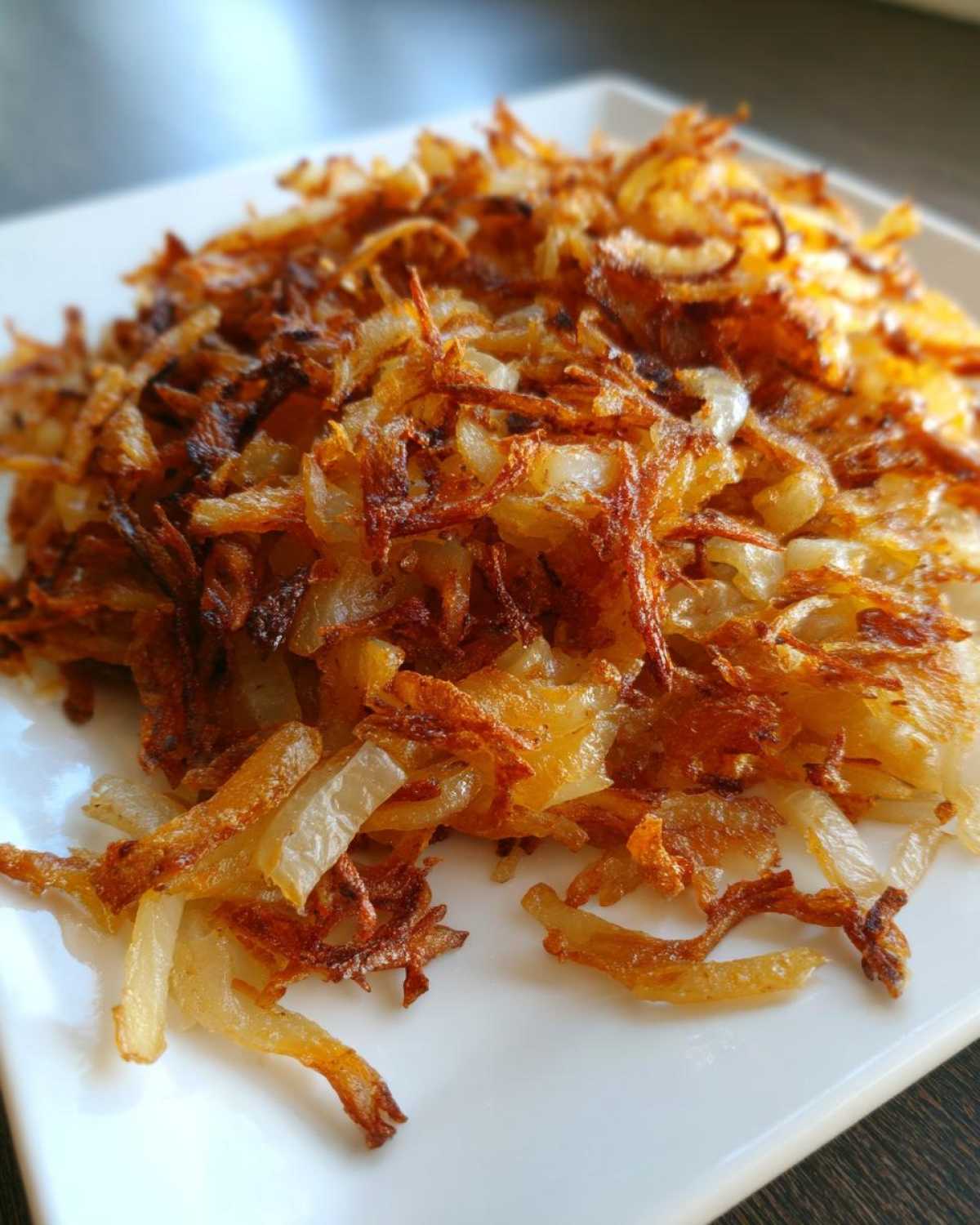 Close-up of perfectly crispy fried potatoes, golden brown and shredded, served on a white plate.