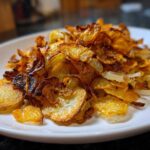 Close-up of thinly sliced, perfectly crispy fried potatoes piled high on a white plate.