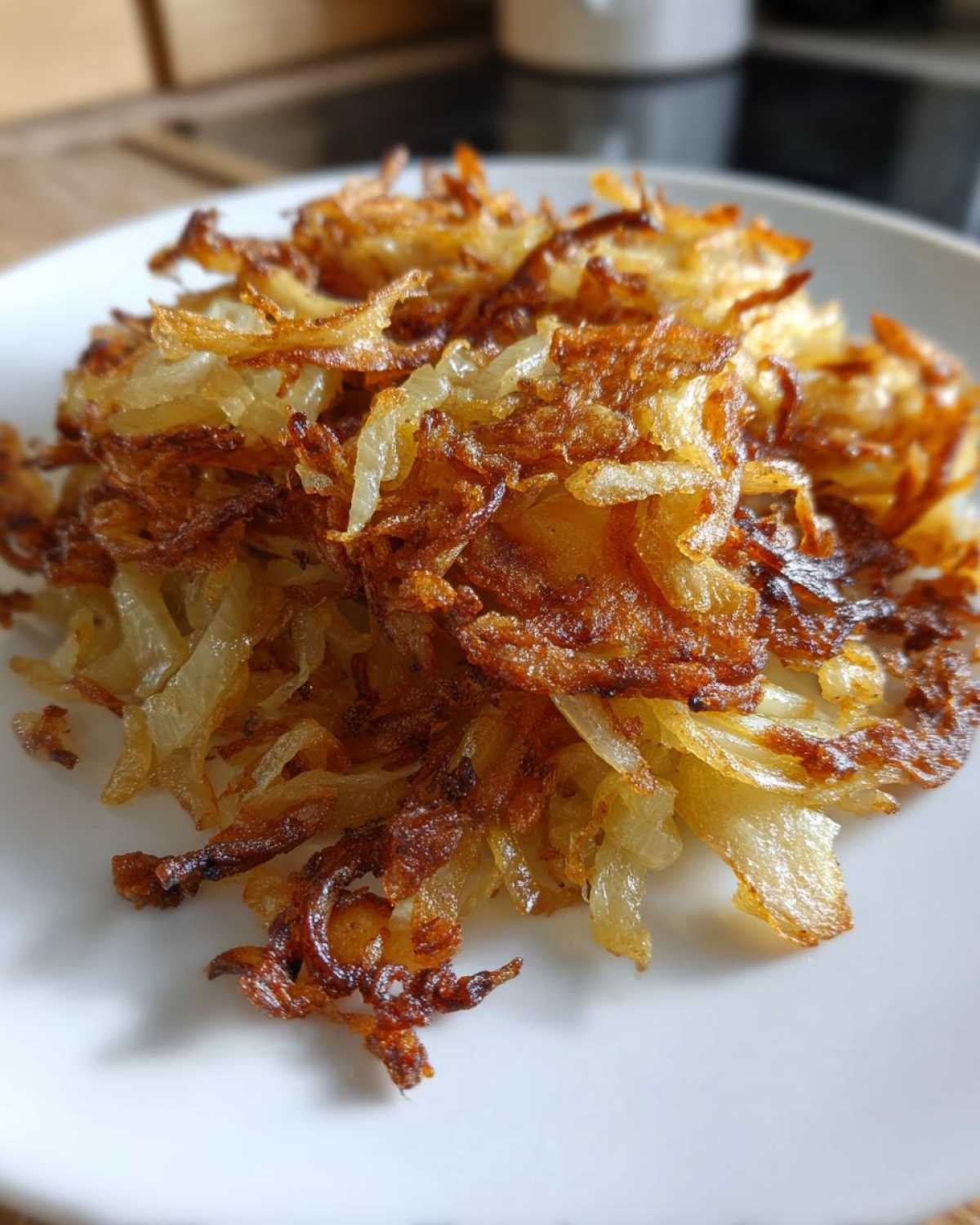 Close-up of perfectly crispy fried potatoes, golden brown and shredded, served on a white plate.