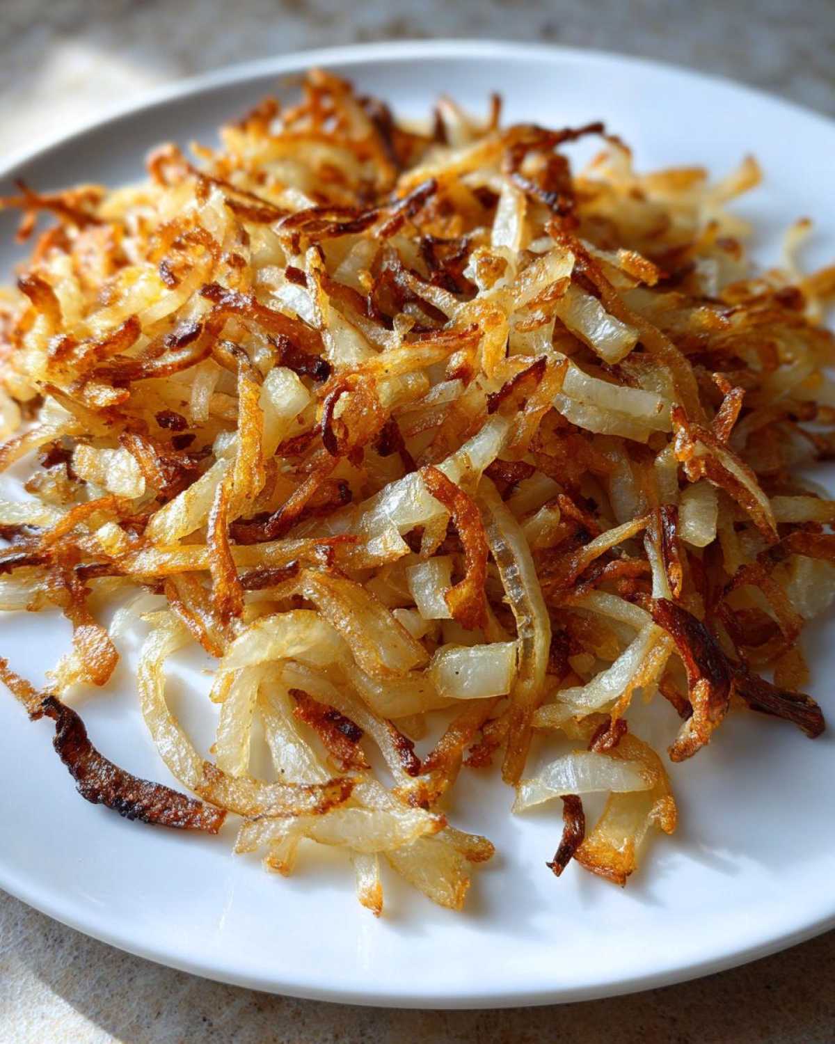 Close-up of perfectly crispy, golden brown fried potatoes piled high on a white plate.