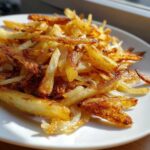 Close-up of a pile of golden brown, crispy fried potatoes served on a white plate.
