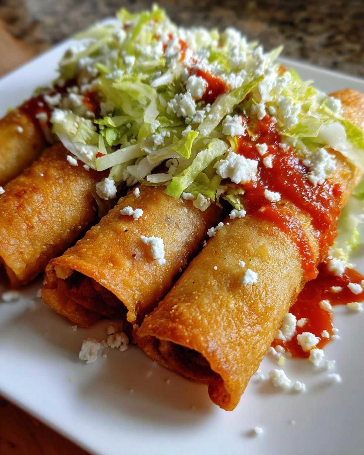 Three crispy, deep-fried potato tacos smothered in red salsa and topped with shredded lettuce and cotija cheese.