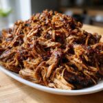 Close-up of a large mound of moist, shredded crock pot pulled pork coated in a dark, savory sauce.