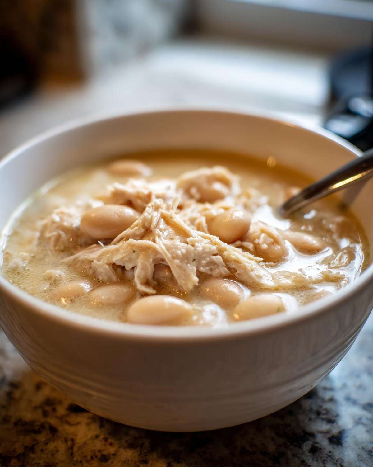 Close-up of a white bowl filled with creamy crockpot white chicken chili, featuring shredded chicken and white beans.