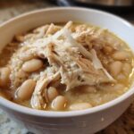 Close-up of a white bowl filled with crockpot white chicken chili, featuring shredded chicken and white beans.