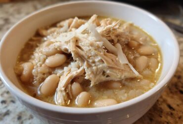 Close-up of a white bowl filled with crockpot white chicken chili, featuring shredded chicken and white beans.