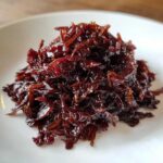 Close-up of a mound of deeply rich, dark brown caramelized onions served on a white plate.