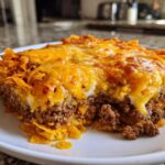 A close-up of a serving of Dorito Casserole featuring a thick layer of seasoned ground beef topped with melted cheddar cheese.