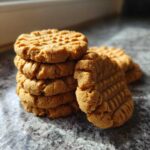 A stack of golden brown Easy Peanut Butter Cookies showing classic crisscross fork marks, resting on a speckled countertop.