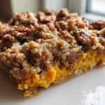 A close-up, macro shot of a single serving of easy sweet potato casserole featuring a bright orange filling and a thick, crunchy pecan crumble topping.