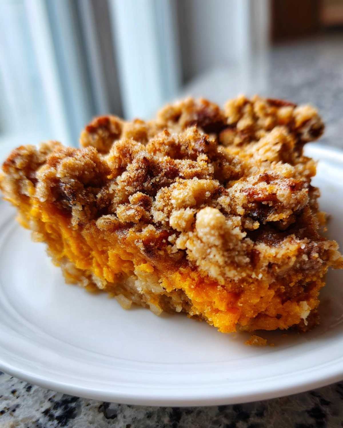 Close-up of a serving of easy sweet potato casserole featuring bright orange filling and a thick, crunchy brown sugar pecan topping.