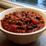 Close-up of a hearty bowl of rich, dark red chili with ground meat and kidney beans, part of the best chili recipe.