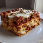 A thick, square slice of homemade lasagna with rich meat sauce and melted white cheese layers.