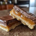 Two decadent squares of homemade twix cookies showing the shortbread base, thick caramel layer, and chocolate topping.