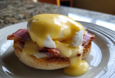 Close-up of a classic eggs benedict featuring a poached egg, ham, and rich hollandaise sauce dripping down.