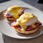 Two servings of classic eggs benedict featuring poached eggs, ham, and rich hollandaise sauce on an English muffin.