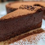 A decadent slice of flourless chocolate torte, rich brown and dusted heavily with cocoa powder.