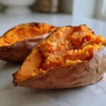 Close-up of a fluffy baked sweet potato split open, revealing bright orange flesh.