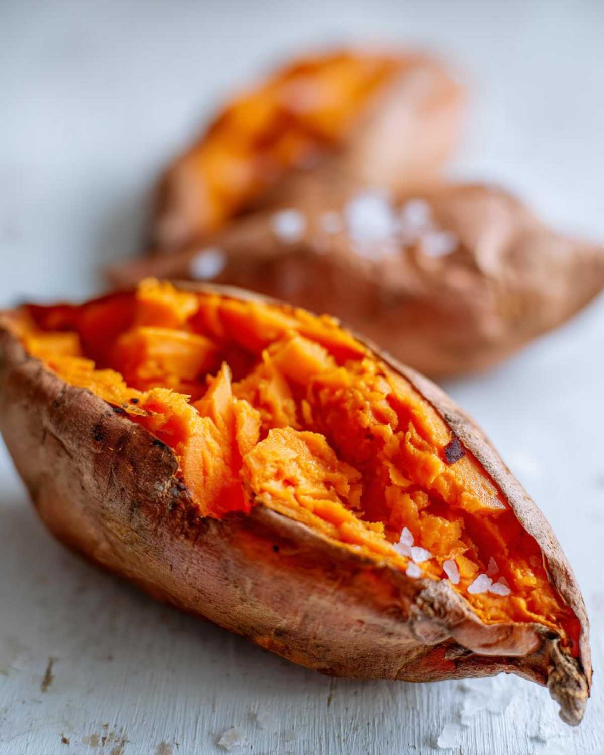 Close-up of a fluffy baked sweet potato split open, sprinkled with coarse sea salt.