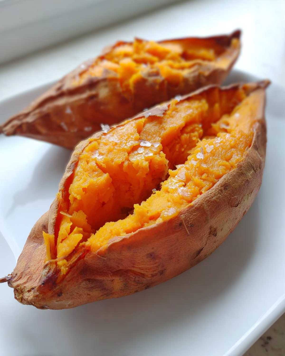 Close-up of a fluffy baked sweet potato, split open and sprinkled with coarse sea salt.