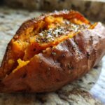 Close-up of a perfectly baked sweet potatoes, split open and topped with salt and herbs.