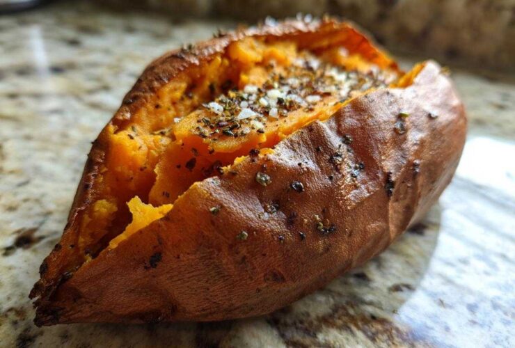 Close-up of a perfectly baked sweet potatoes, split open and topped with salt and herbs.