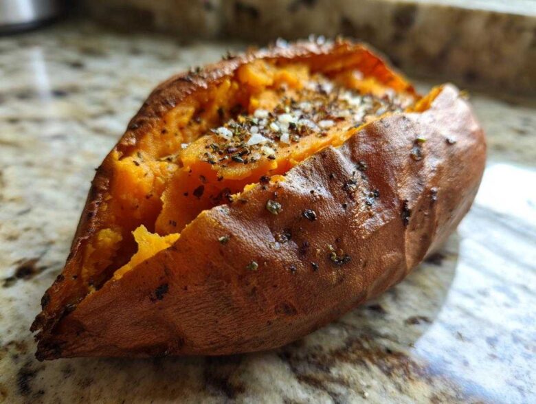 Close-up of a perfectly baked sweet potatoes, split open and topped with salt and herbs.