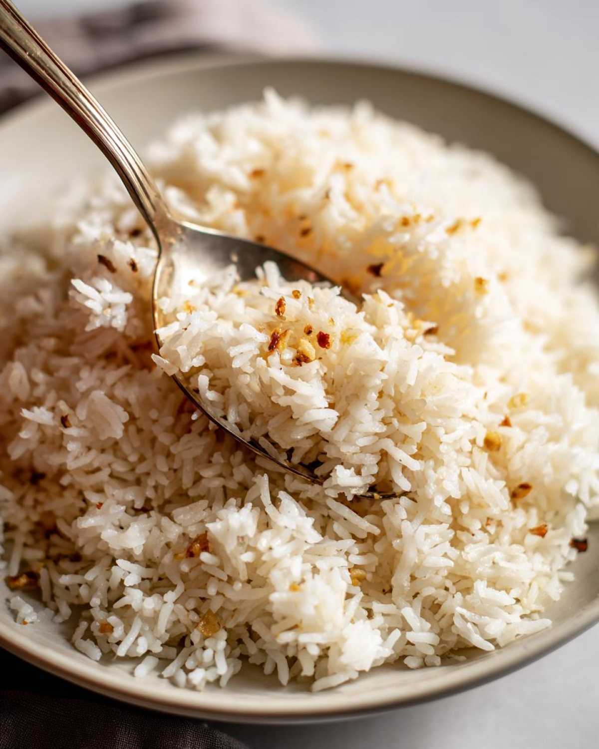 Close-up of fluffy white butter rice in a bowl, being scooped with a silver spoon, showing browned bits of butter.