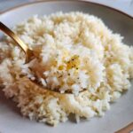 Close-up of fluffy butter rice being lifted on a gold spoon, seasoned with pepper and herbs.