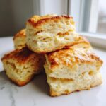 Close-up of fluffy buttermilk biscuits stacked on a marble surface, showing their flaky layers and golden tops.