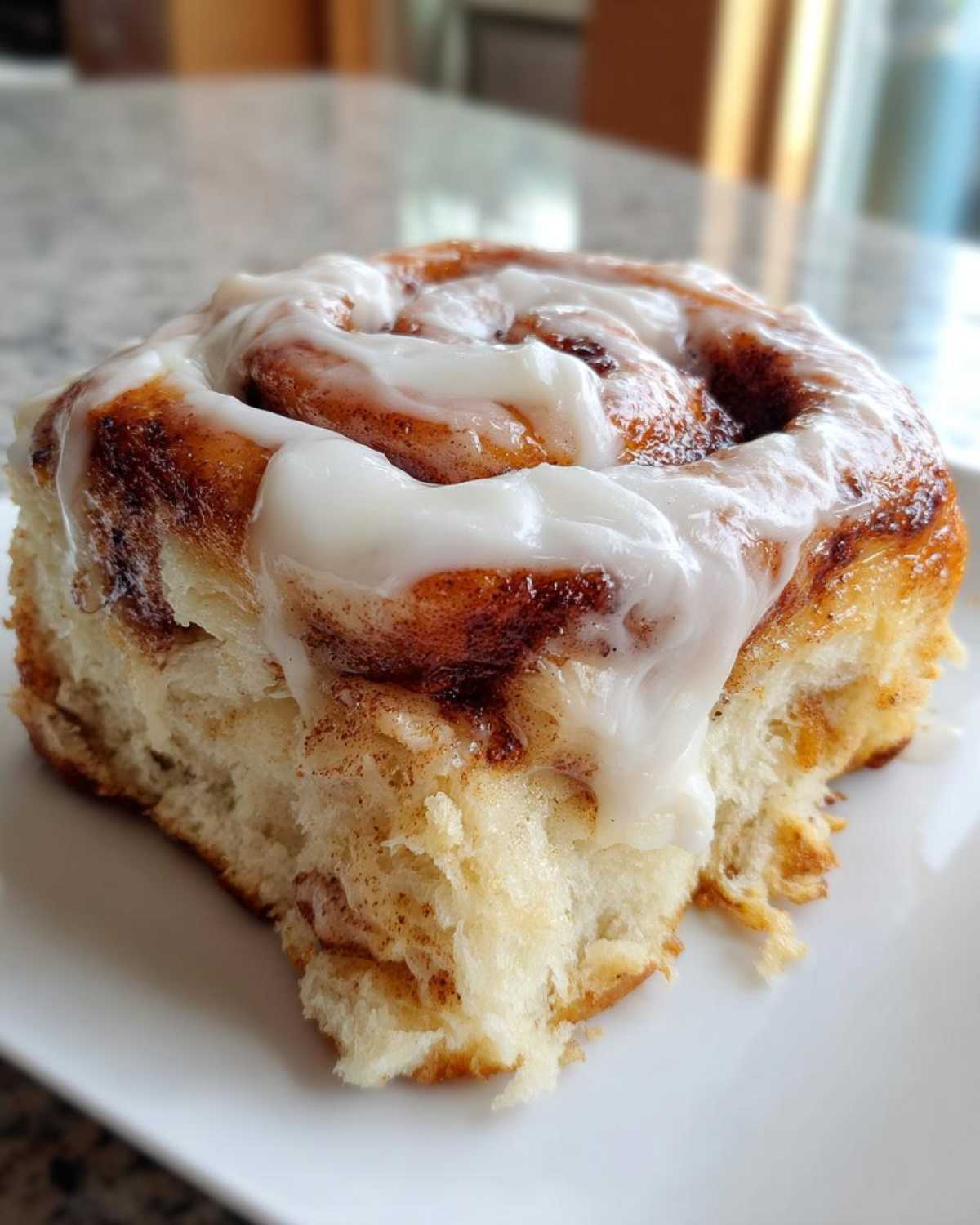 A close-up shot of a single, fluffy cinnamon roll generously topped with white cream cheese icing.