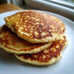 A close-up of three fluffy coconut flour pancakes stacked on a white plate.
