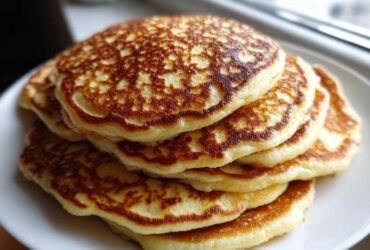 A tall stack of fluffy coconut flour pancakes with golden brown, lacy edges served on a white plate.