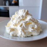 A generous, fluffy mound of freshly whipped cream cheese frosting piled high on a white plate.