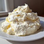 A large, fluffy mound of freshly whipped cream cheese frosting sitting on a white plate.