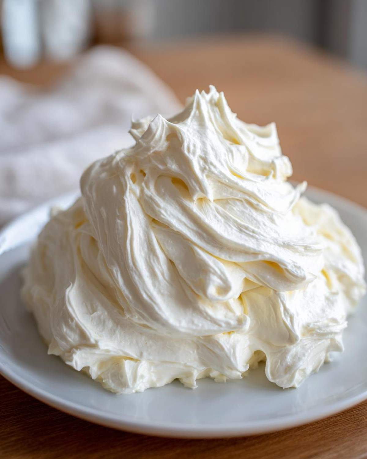 A large, perfectly piped mound of white, fluffy cream cheese frosting sitting on a light blue plate.