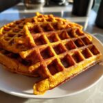 Close-up of a stack of fluffy, golden-brown pumpkin waffles glistening under sunlight.
