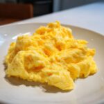 Close-up of perfectly fluffy scrambled eggs with a creamy texture served on a white plate.